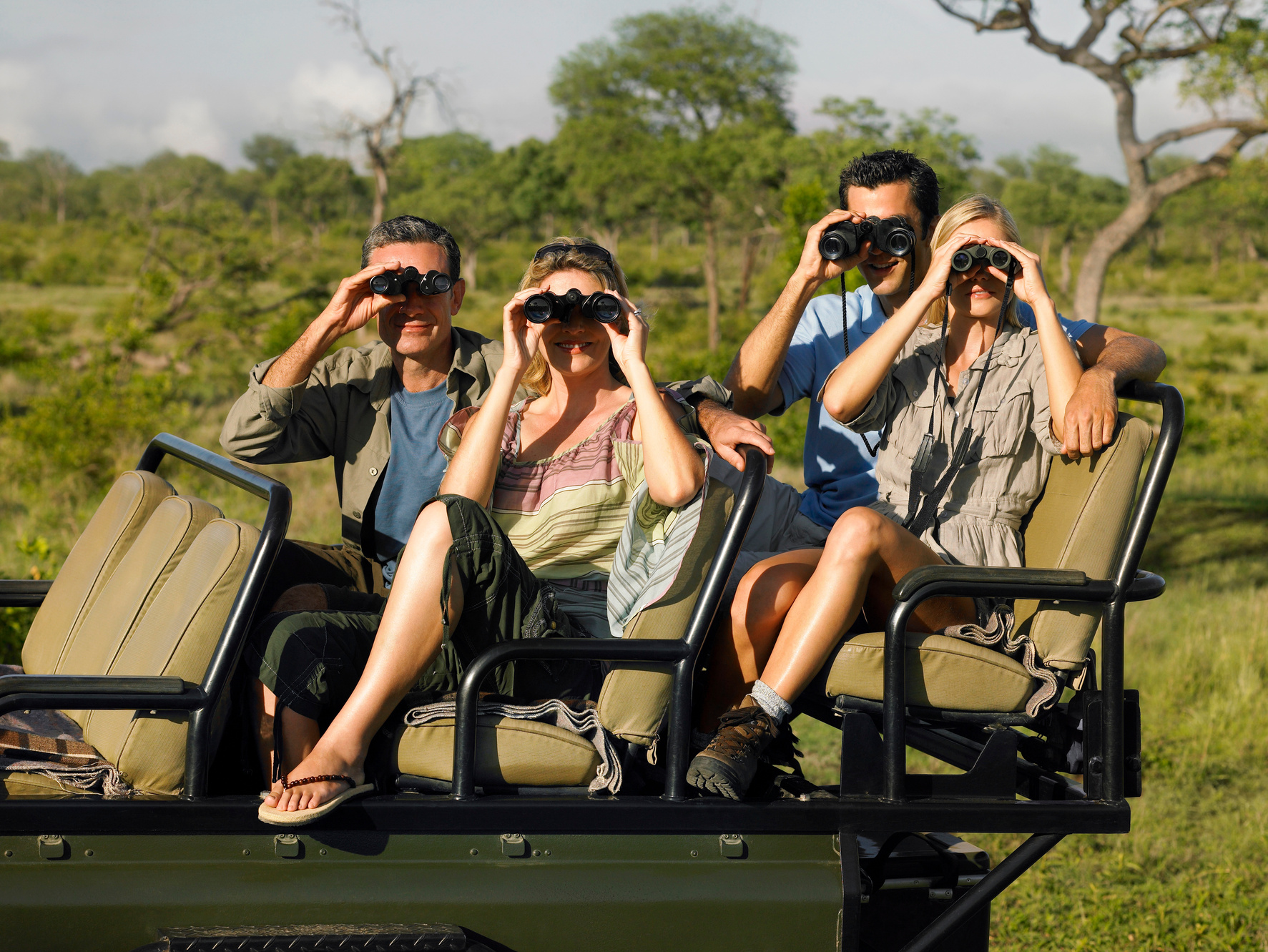 Group of tourists on safari sitting in jeep looking through binoculars